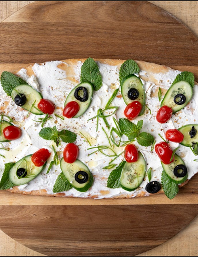 Manakish labné, concombre, tomates cerises, olives et menthe fraîche, servi sur planche en bois